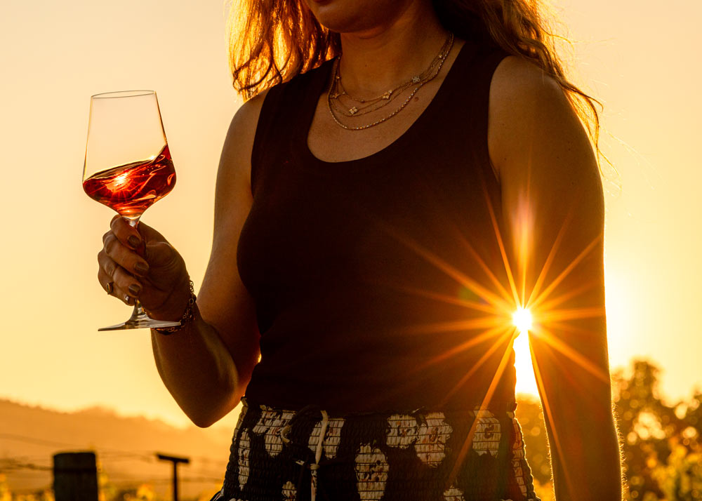 A woman enjoying the beautiful lighting of golden hour in Napa Valley, a glass of Grgich Hills Estate Rosé in hand.