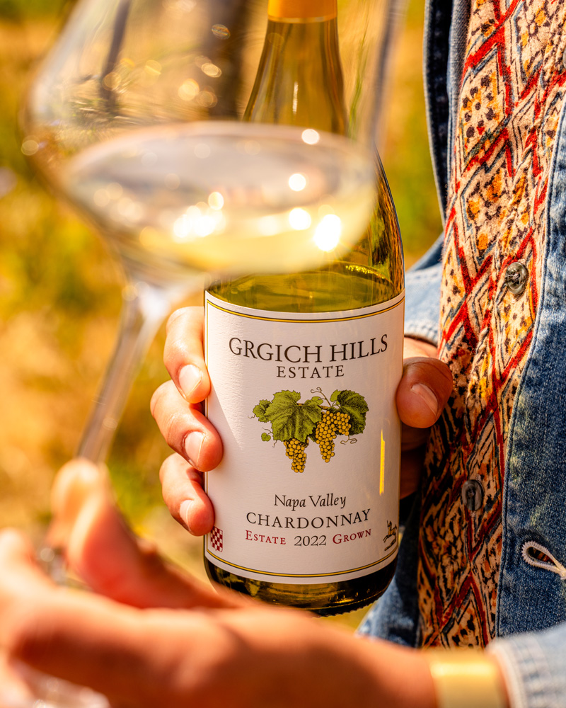 A young man holds a bottle of Napa Valley Chardonnay close as he swirls a glass of the wine.