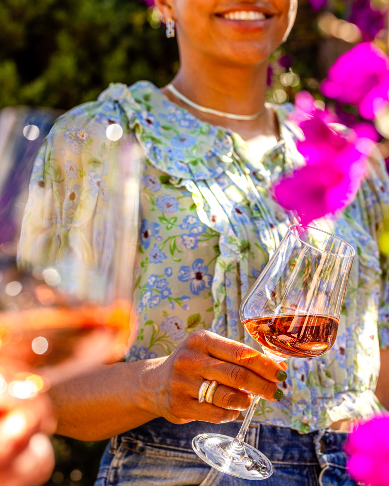 A young woman enjoys a glass of Napa Valley Rose with friends among brightly blooming bougainvillea.