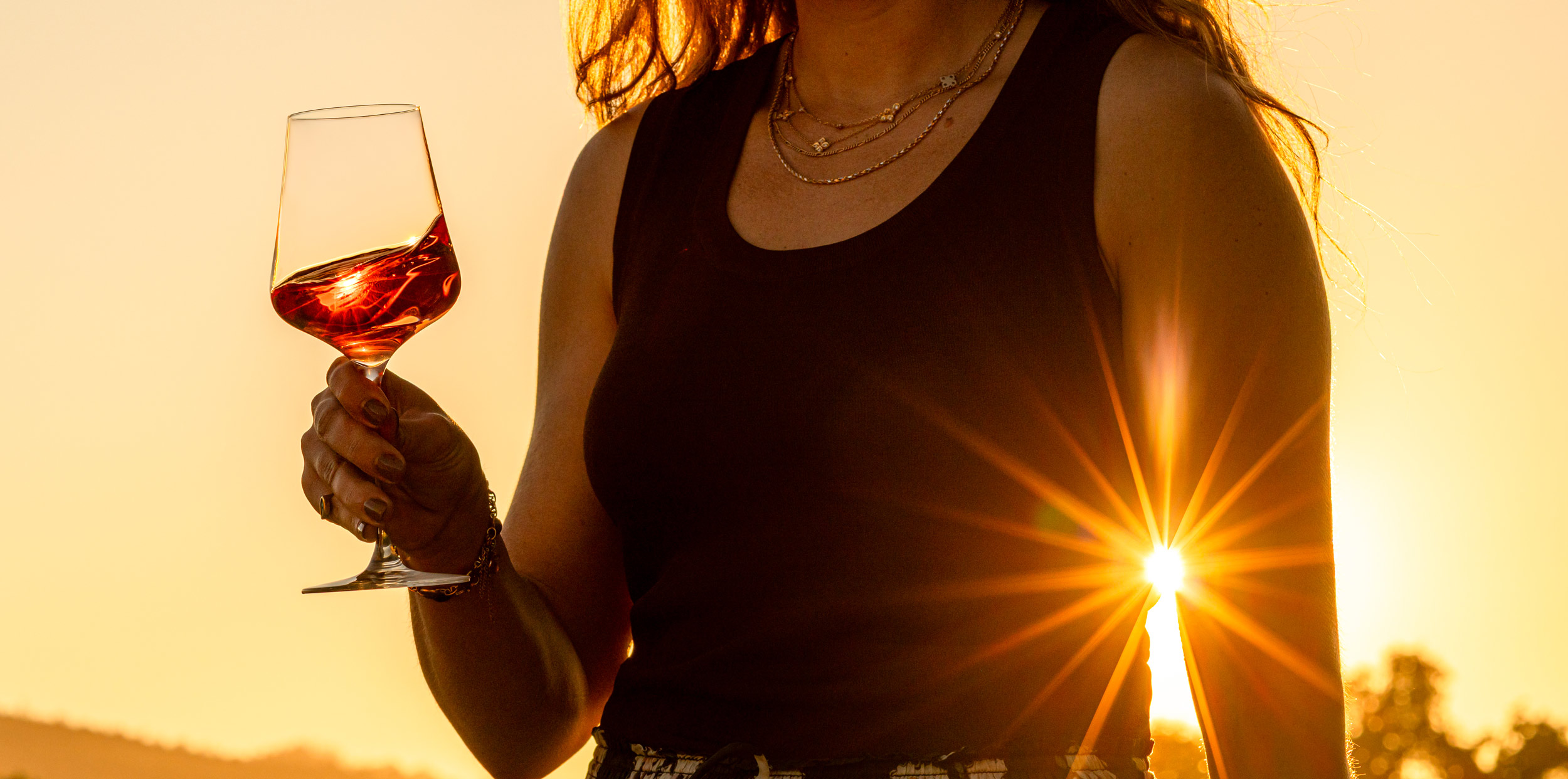 A woman enjoying the beautiful lighting of golden hour in Napa Valley, a glass of Grgich Hills Estate Rosé in hand.