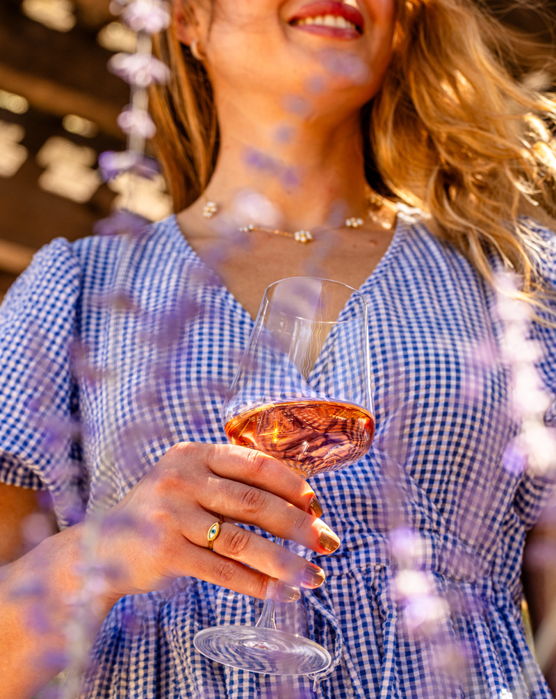 A young woman dressed in gingham delicately clutches a glass of Napa Valley Rosé wine.