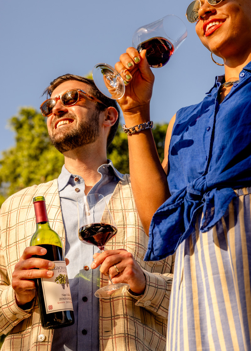 A pair of young adults basking in the afternoon sun, wineglasses in hand and an open bottle of Napa Valley Zinfandel ready to pour.